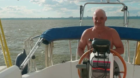 Bald captain sits at steering wheel of sailing yacht and talks. Stock Footage 142250171
