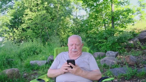 Bald elderly man holds modern smartphone and taps on screen Stock Footage 136776190