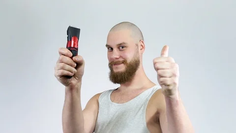Bald guy with a beard and a clipper in his hands, shaving himself.Thumbs up Stock Footage 122503783