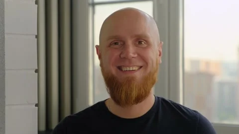 A bald guy with a red beard smiles into the camera with a friendly smile. Video stock 142580865