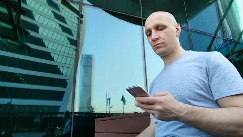 Bald guy with smartphone nods to passing person 库存影片 201891821