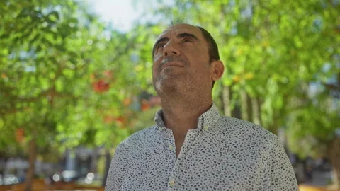 Bald hispanic man in a patterned shirt gazing upward in a lush urban park o.. Stock Footage 277863643