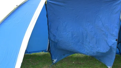 A bald man with a beard comes into a blue tent, set on the grass. Stock Footage 125919049