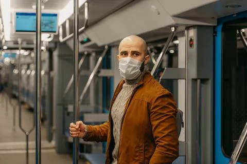 A bald man with a beard in a face mask is holding the handrail in a subway ca Stock Photos