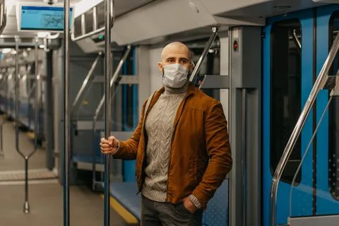 A bald man with a beard in a face mask is holding the handrail in a subway ca Stock Photos