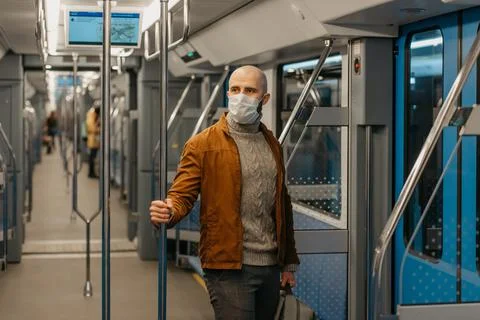 A bald man with a beard in a face mask is holding the handrail in a subway ca Stock Photos