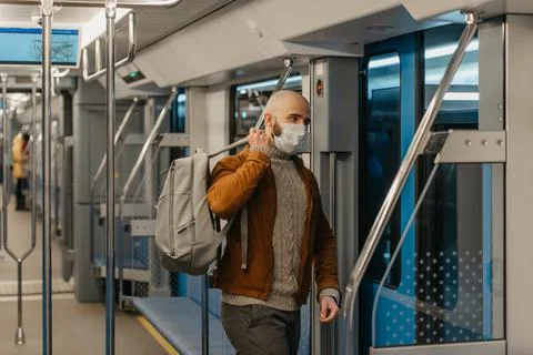 A bald man with a beard in a face mask is putting on a backpack in a subway c Stock Photos