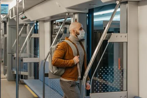 A bald man with a beard in a face mask is leaving a subway car. Stock Photos