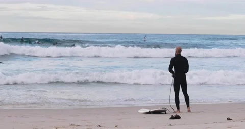 Bald man with beard prepares for surf during sunrise Stock Footage 137624302
