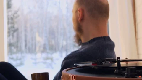 A bald man with a beard sits on the sofa, drinks coffee and listens to classical Stock Footage 195004248