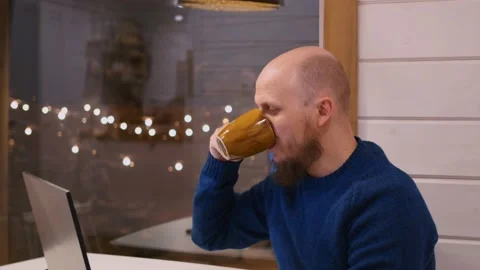 A bald man with a beard sits at a table working remotely from home after his Stock Footage 171791497