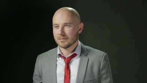 Bald man with a beard in a suit looks to the side and corrects red tie. on a Stock Footage 72107751