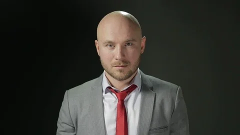 Bald man with a beard in a suit looks to the camera and corrects red tie. on a Stock Footage 72108157