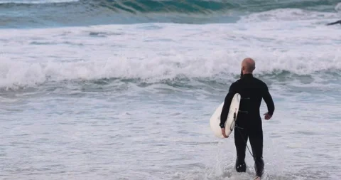 Bald man with beard walks into the surf carrying his surfboard 動画素材 137624403
