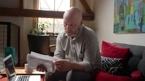 Bald man with a beard wonders how he is going to pay his stack of bills Video stock 133291369