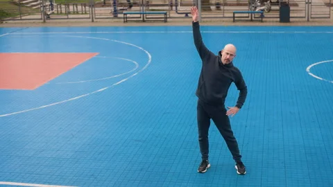 Bald man in black tracksuit doing morning exercises alone on an empty outdoor Stock Footage 306099696