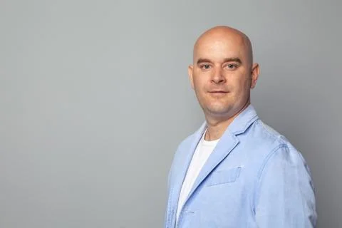 Bald man in a blue jacket against a gray wall Stock Photos