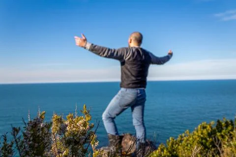 Bald man on a cliff edge, spread his arms against sea view. Happy and confident Stock Photos