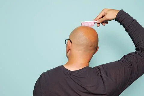 Bald man combs the back of his head with a baby comb, on a turquoise background Stock Photos