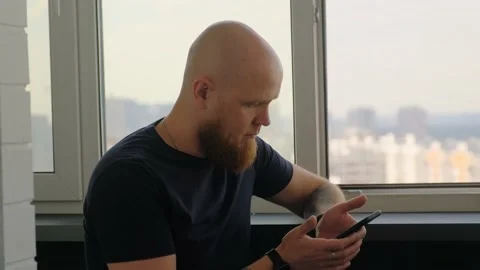 A bald man dials a number on his smartphone and brings it to his ear. Stock Footage 142581634