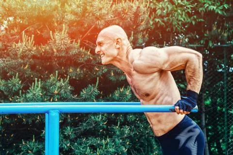 Bald Man doing push ups on parallel bars in a park Stock Photos