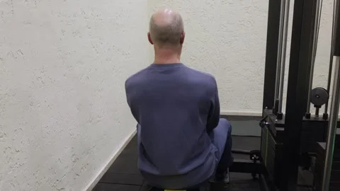 Bald man doing seated cable row exercise on gym machine with weight stack Stock Footage 324755625