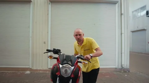 A bald man driving instructor in a yellow T-shirt drives a red moped into the Stock Footage 249234977