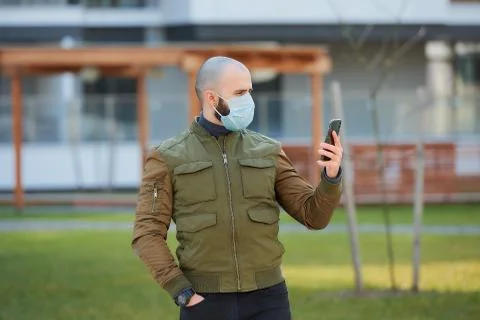 A bald man in a face mask checking his smartphone on a cozy street. Stock Photos