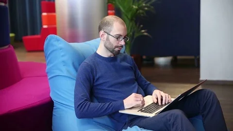 Bald man with glasses working on laptop with phone Stock Footage 69977086