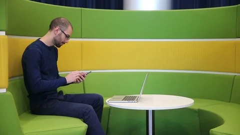 Bald man with glasses working on laptop with talk phone Stock Footage 69977148