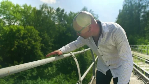 A bald man going along on an abandoned railway bridge and touches the railing Stock Footage 114980751