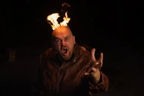 Bald man in a leather jacket with a burning head on a dark background. Stock Photos