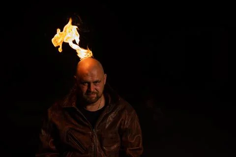 A bald man in a leather jacket with a burning head grins. Stock Photos