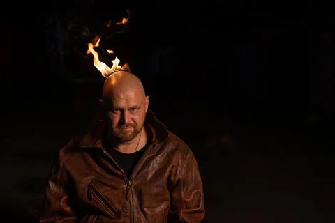 A bald man in a leather jacket with a burning head grins. Stock Photos