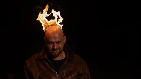 A bald man in a leather jacket with a burning head grins. Stock Photos