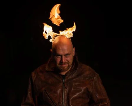 A bald man in a leather jacket with a burning head grins. Stock Photos