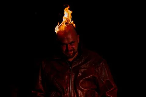 A bald man in a leather jacket with a burning head grins. Stock Photos