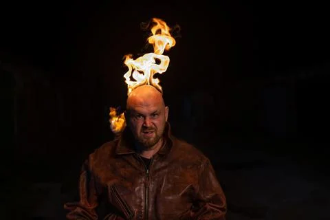 A bald man in a leather jacket with a burning head grins. Stock Photos