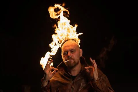 Bald man in a leather jacket with a burning head on a dark background. Stock Photos