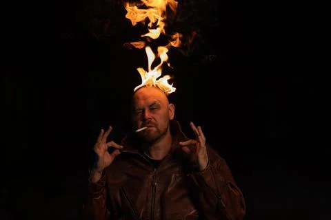 Bald man in a leather jacket with a burning head on a dark background. Stock Photos