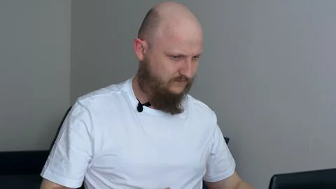 A bald man with a middle-aged beard sits in front of a laptop and is trained Stock Photos