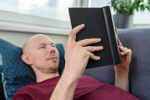 Bald man reading book on couch Stock Photos