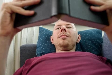 Bald man reading book on couch Stock Photos