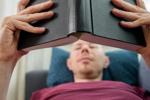 Bald man reading book on couch Stock Photos