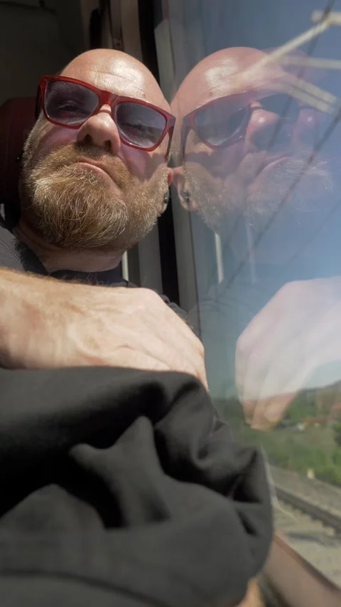 Bald man with red goatee sleeping against train window 動画素材 334775660