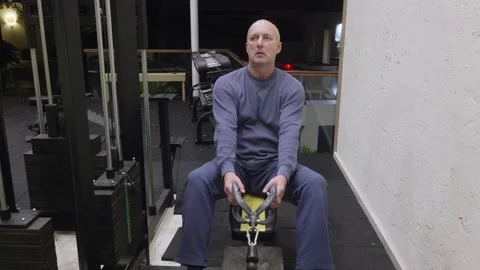 Bald man sitting on yellow bench using cable machine in modern home gym Stock Footage 324755704