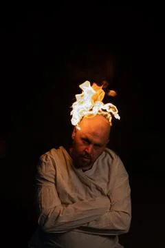 Bald man in a straitjacket with a burning head on a dark background. Stock Photos
