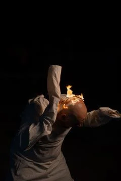 Bald man in a straitjacket with a burning head on a dark background. Stock Photos