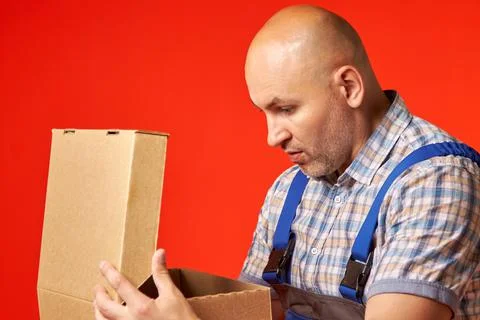 Bald man in work clothes opens an empty cardboard box and is very surprised Stock Photos