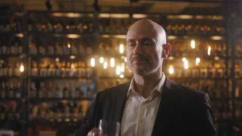 A bald middle-aged man in a black suit and white shirt drinks beer from a large Stock Footage 305181916